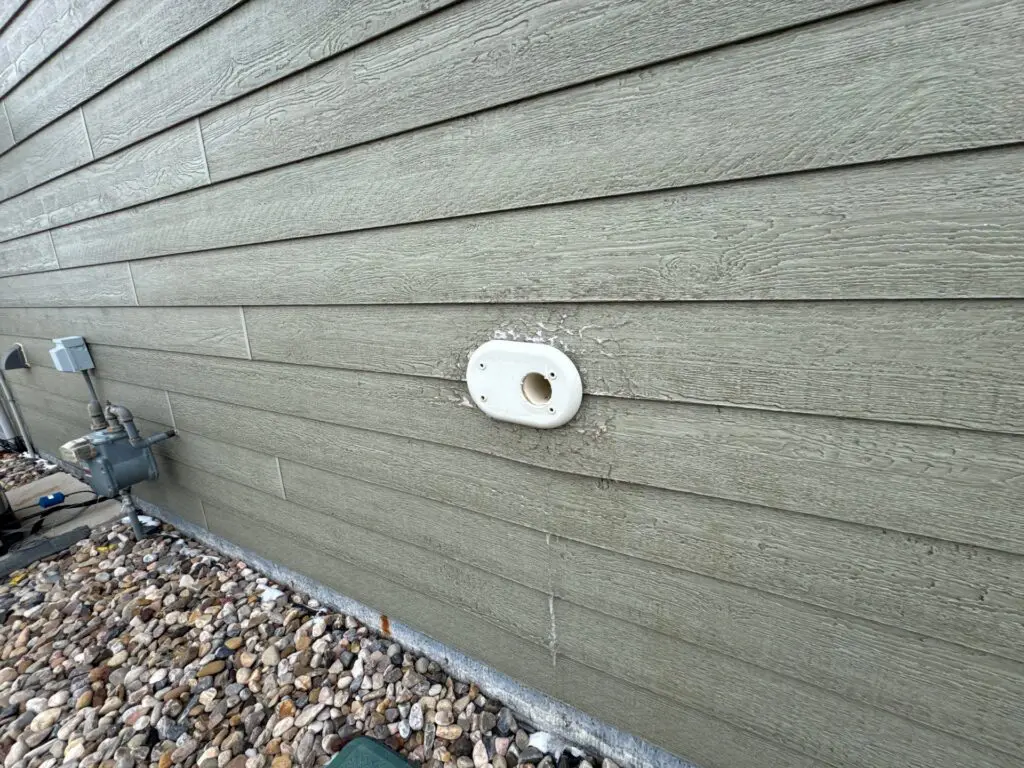 Angled view of siding damage around intake/exhaust pipe for warranty claim