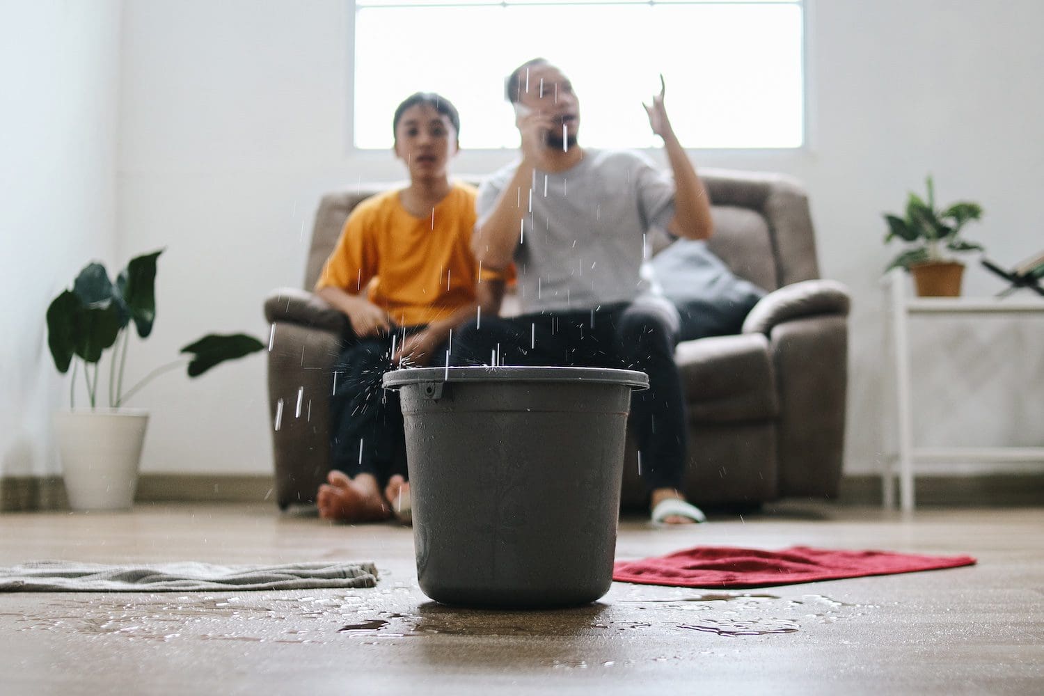 Bucket in living room catching water while owners are on the phone