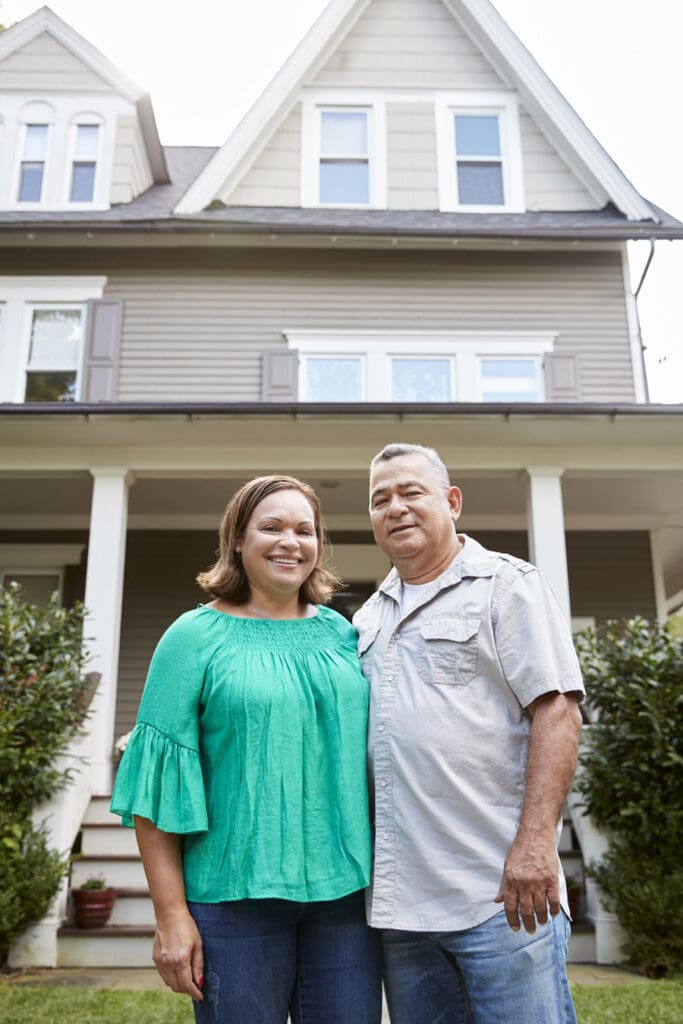 Smiling Couple in Front of Their Well-Maintained Home